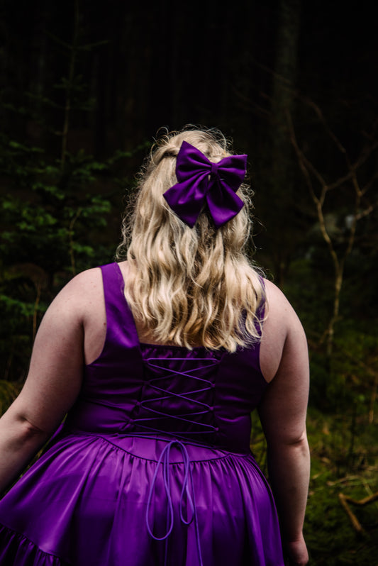 Woman in amethyst purple dress wearing a matching hair bow from the gemstone collection