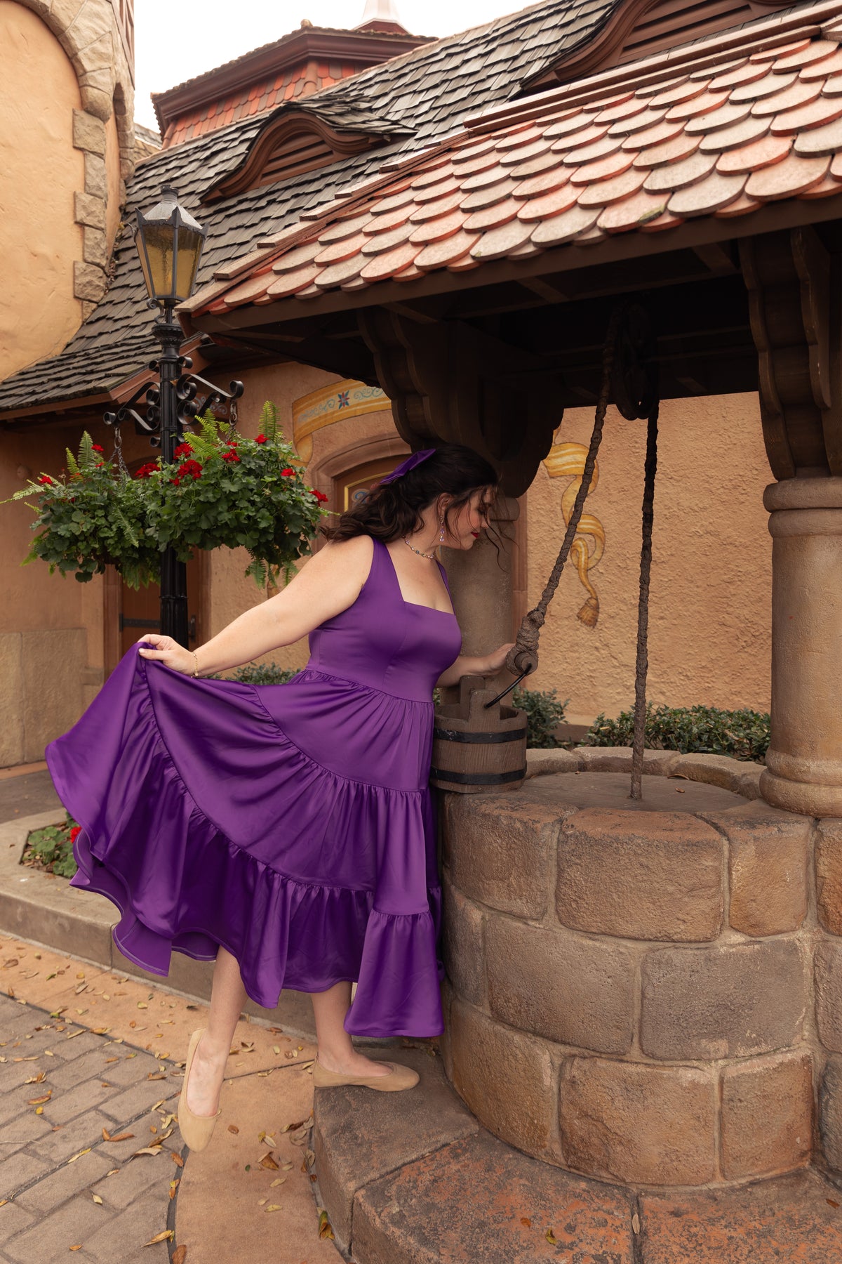 Woman in Amethyst Purple Madonna Dress posing next to a wishing well in a village setting
