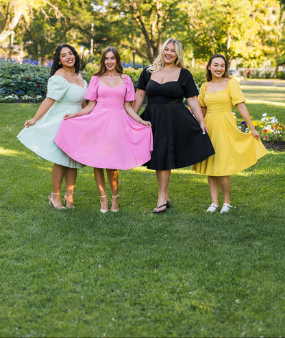 Four women in colorful dresses standing on grass with trees in the background