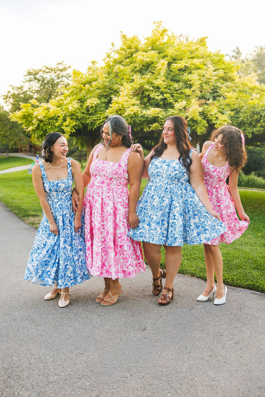 Four women in floral dresses standing on a path with trees in the background