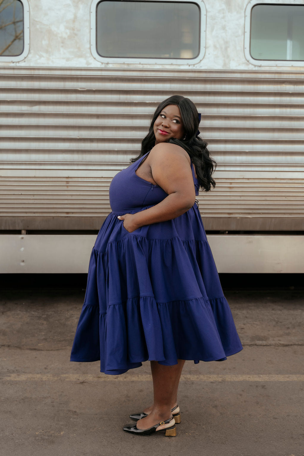 Woman in a blue dress standing in front of a vintage trailer.