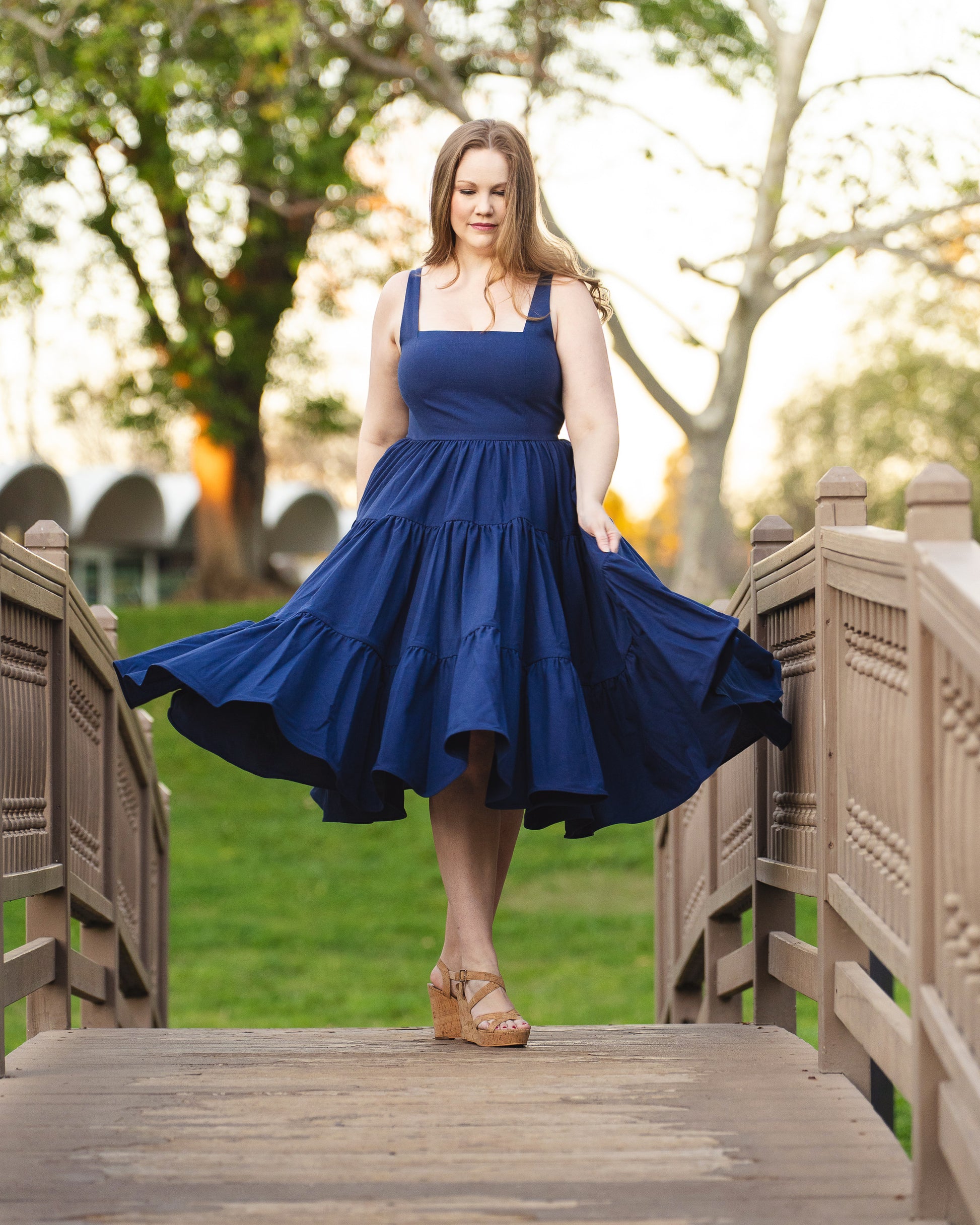 Woman in a blue dress standing on a wooden bridge with trees in the background