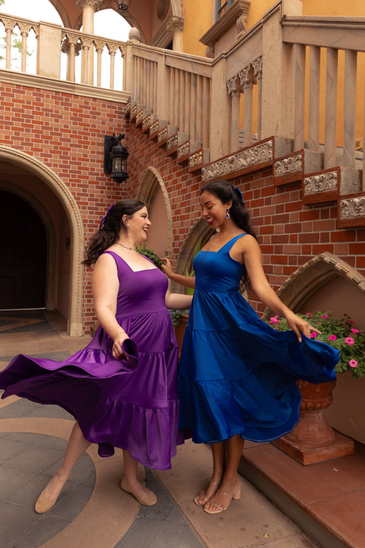 Two women twirling in Sapphire Blue and Amethyst Purple Madonna Dresses in a castle courtyard